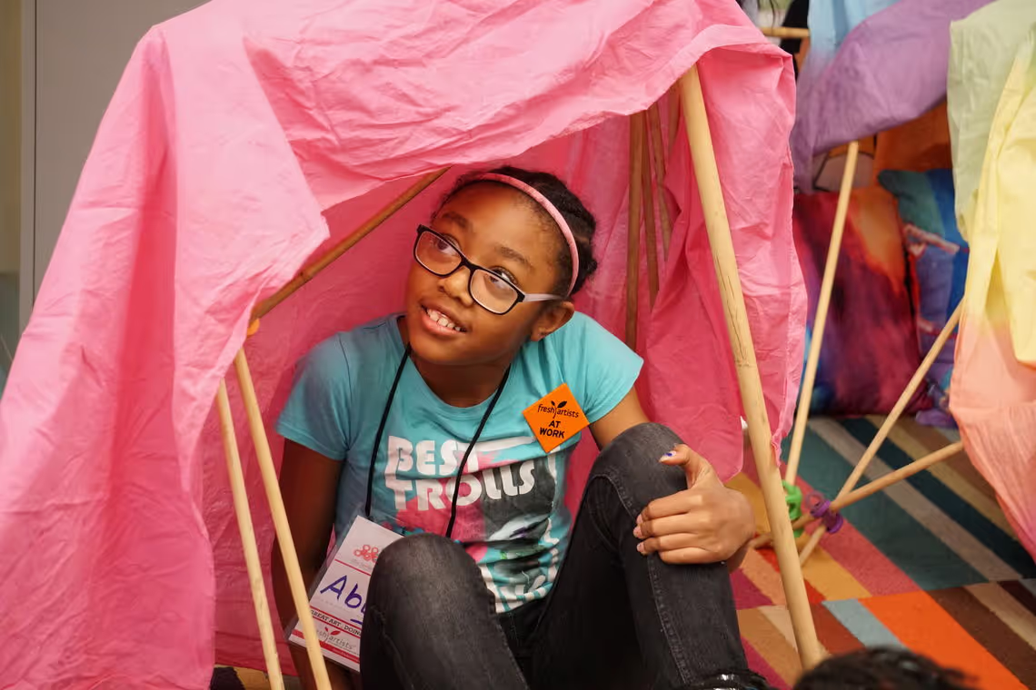 A young girl sitting on the floor in front of a pink tent